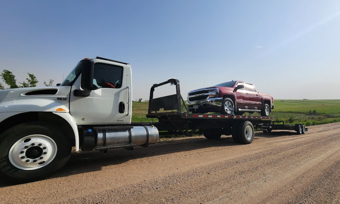 A tow truck is towing a red car on a trailer.