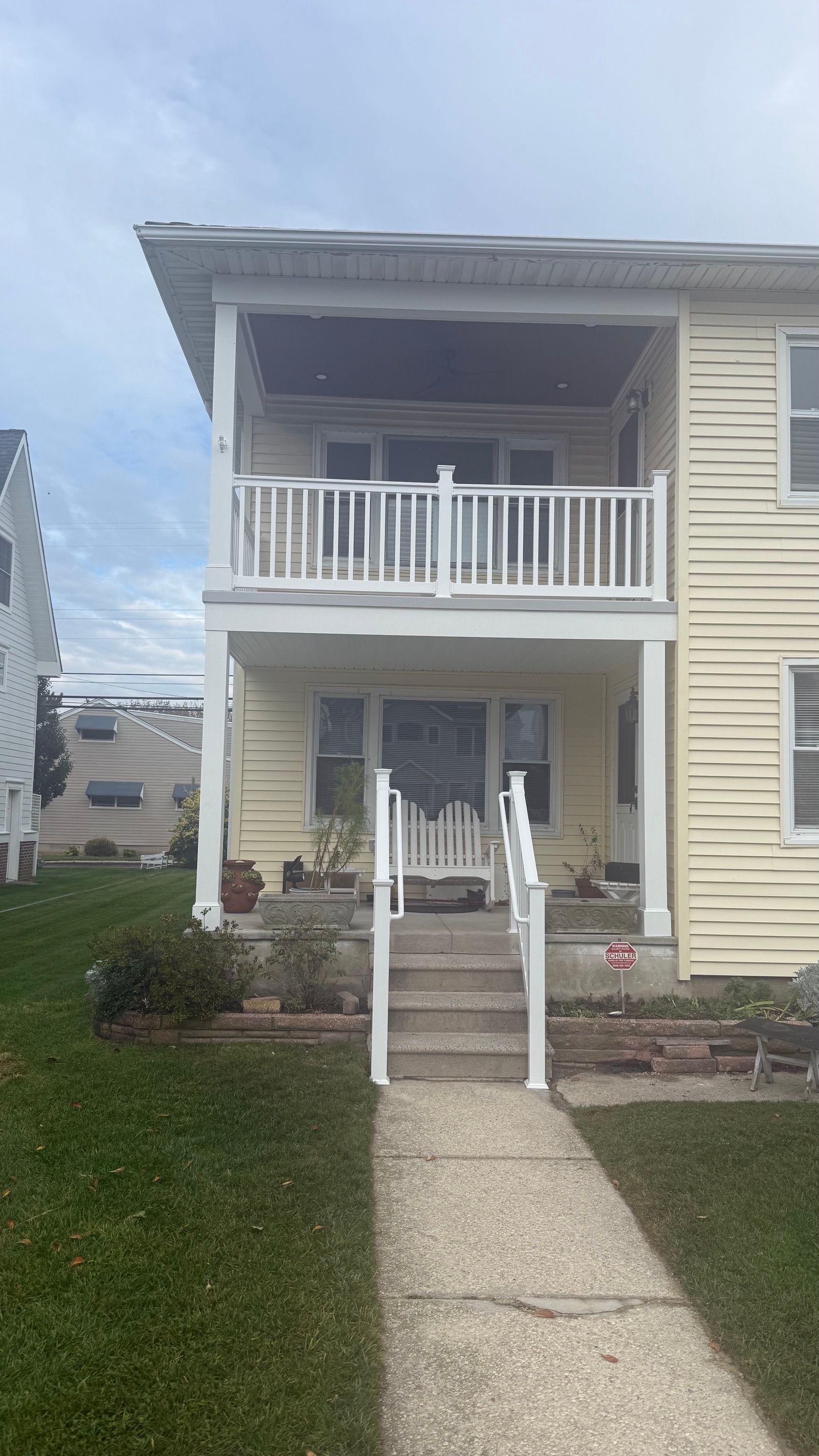 Two-story beige house with a front porch, stairs, and a concrete walkway leading to the entrance.