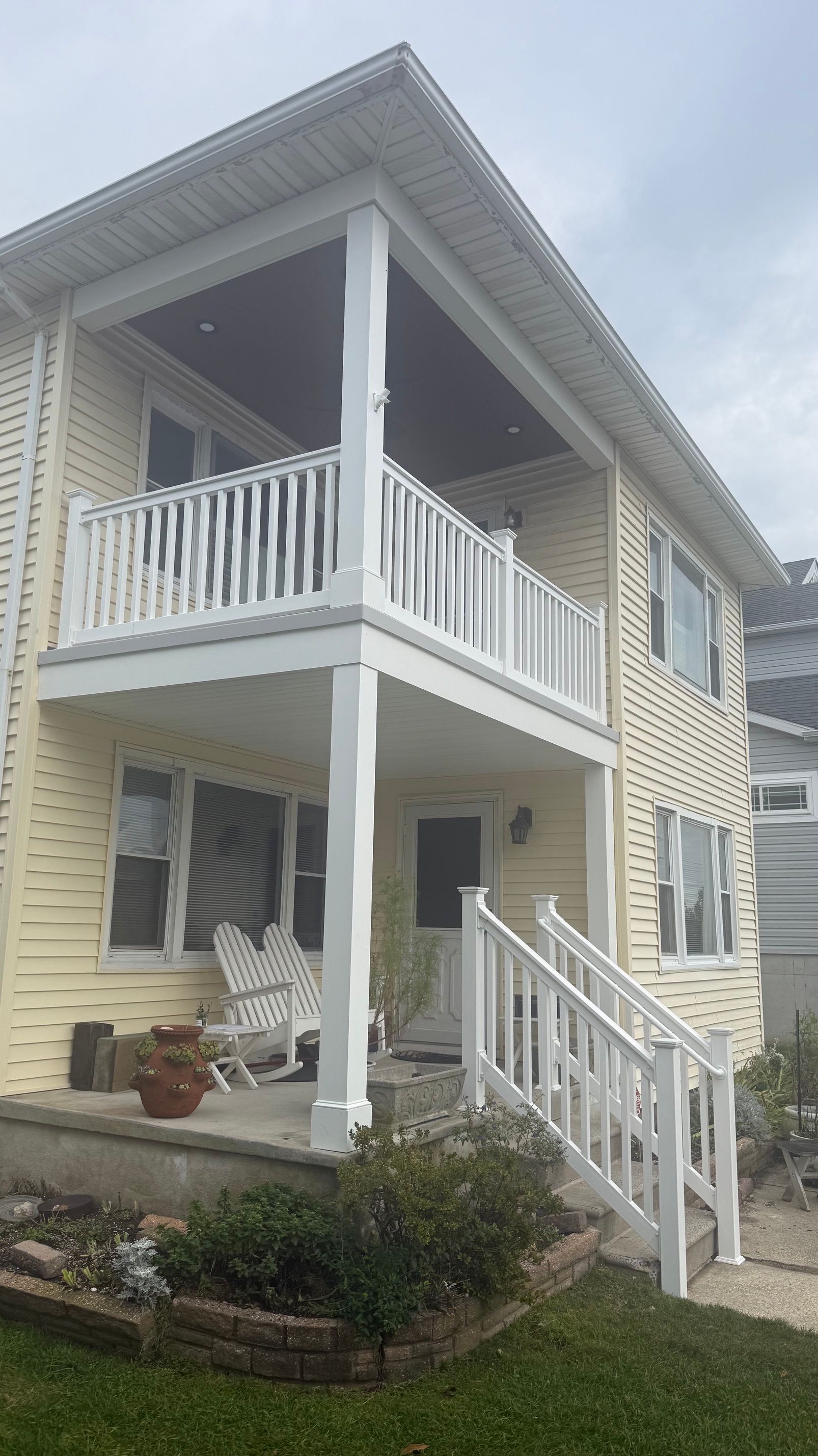Two-story white house with wraparound porch, balcony, and front steps in a residential setting