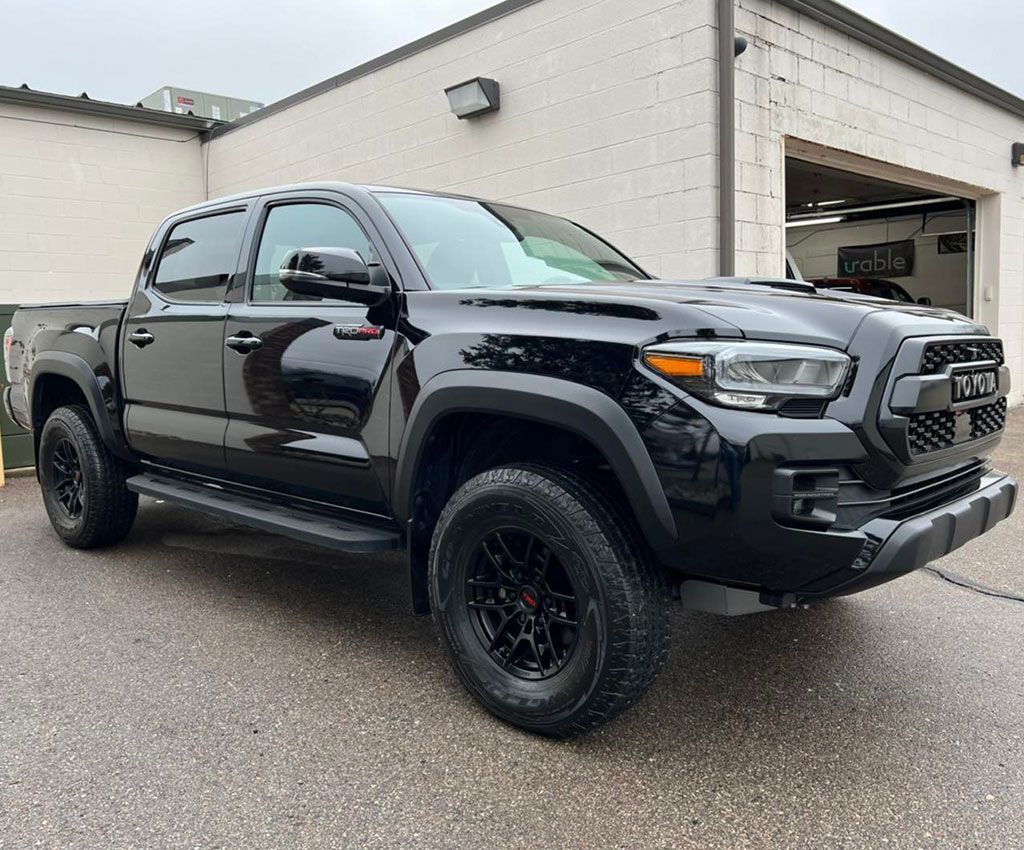 Black Toyota Tacoma pickup truck parked near a building, on wet pavement.