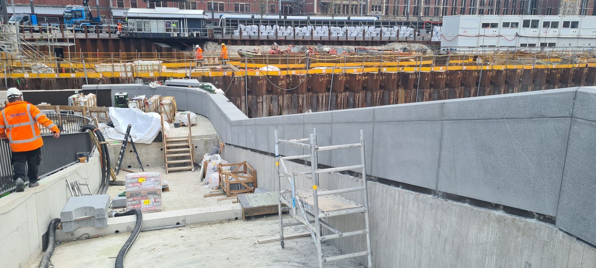 Een bouwplaats met steigers en een trein op de achtergrond.