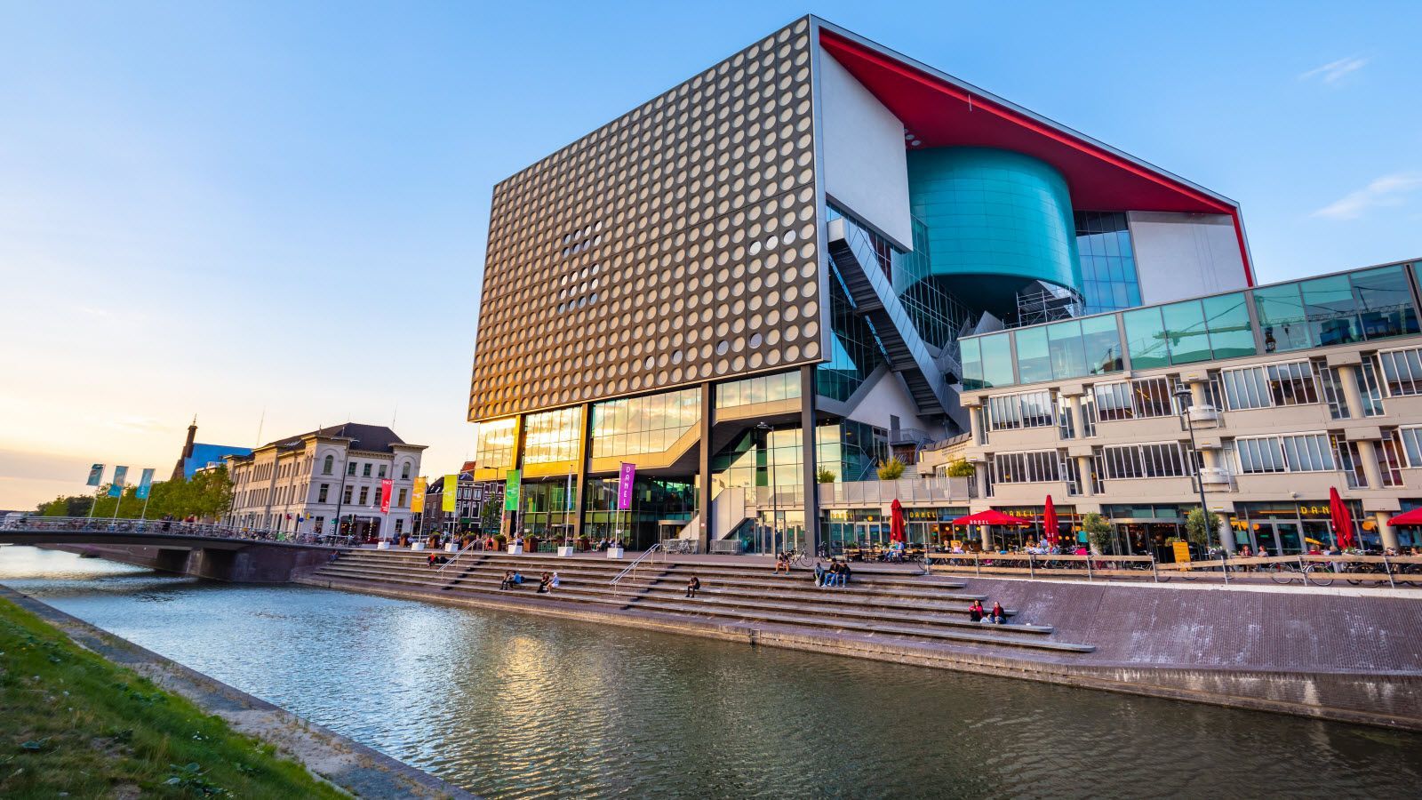 Een groot gebouw met een rood dak staat naast een rivier.