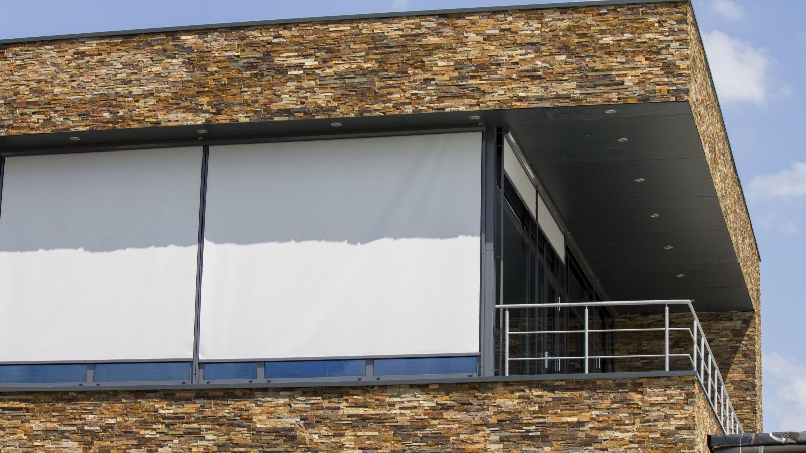 Een gebouw met een balkon en een groot raam met jaloezieën.