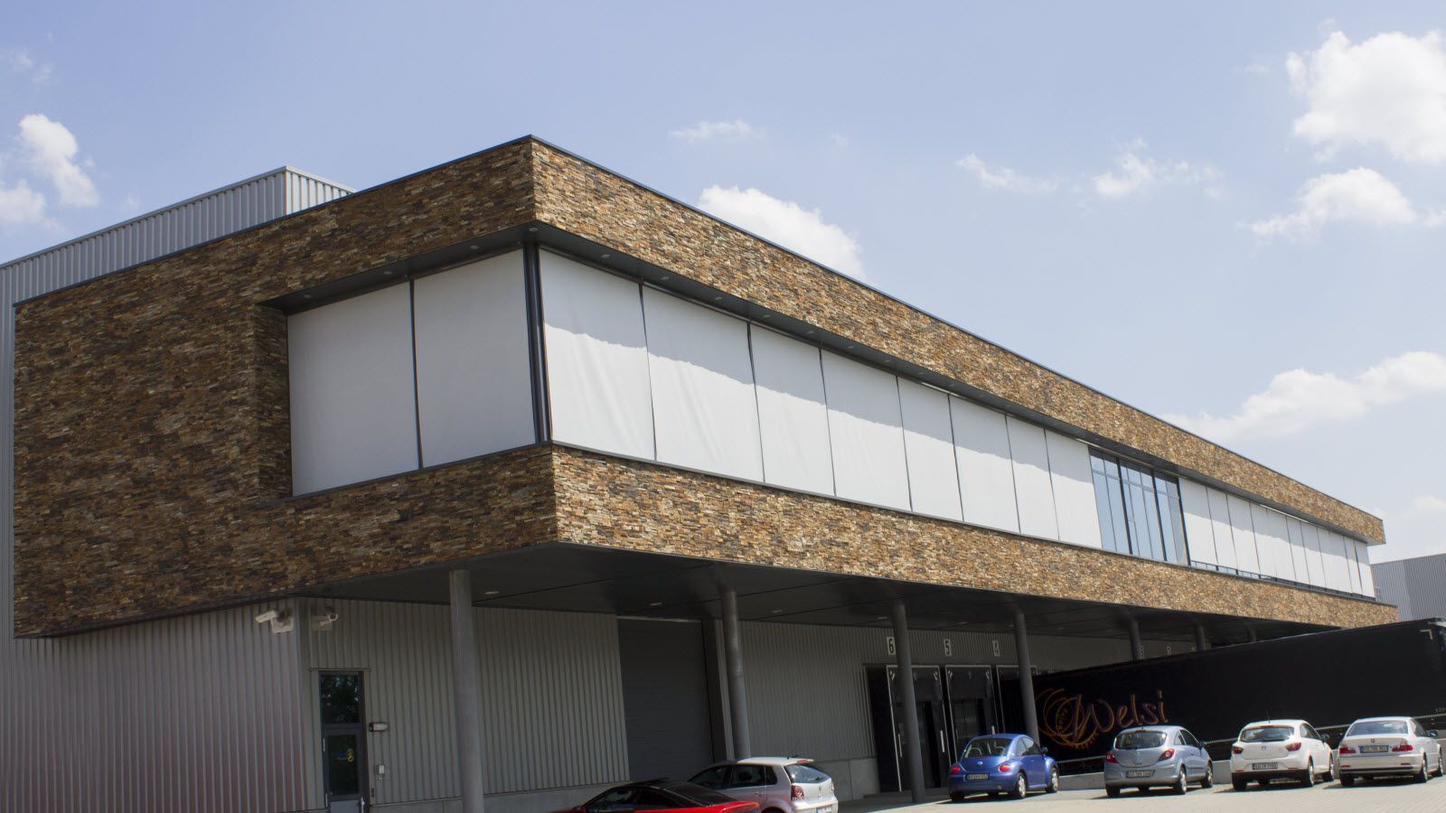 Een groot gebouw met veel ramen en auto's ervoor geparkeerd.
