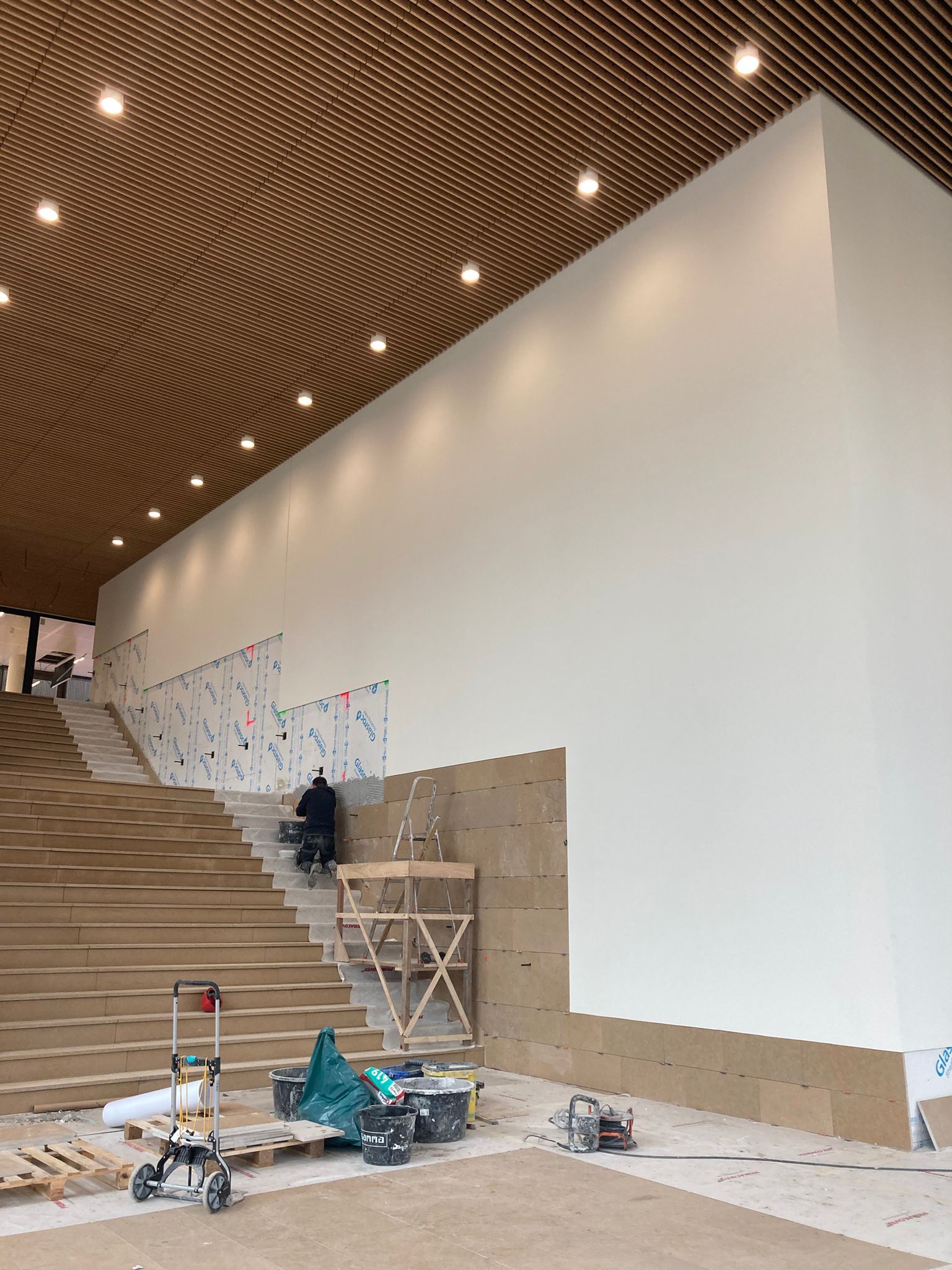In een grote ruimte met een houten plafond wordt een trap gebouwd.