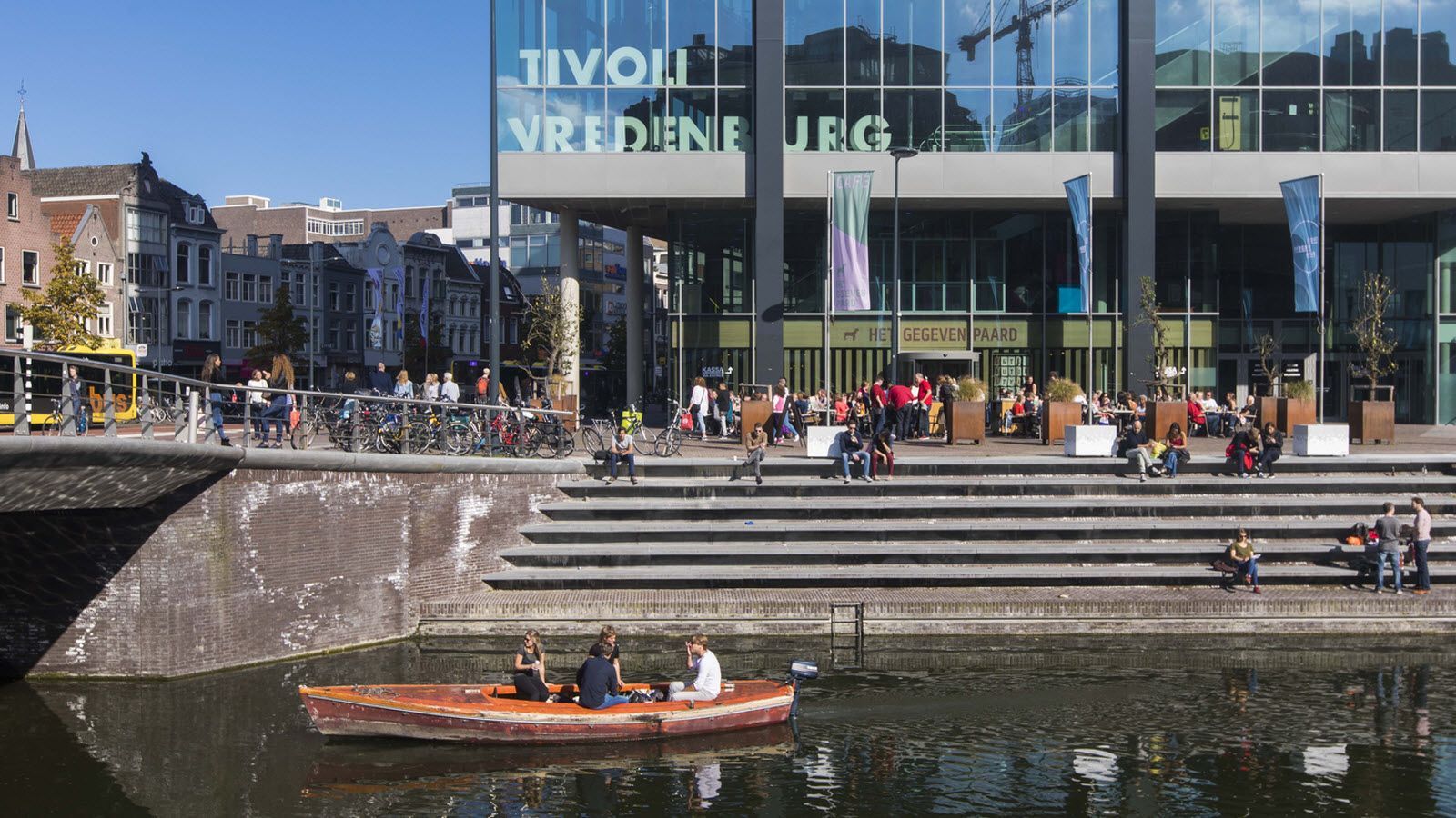 Een groep mensen zit in een boot op een rivier voor een gebouw.