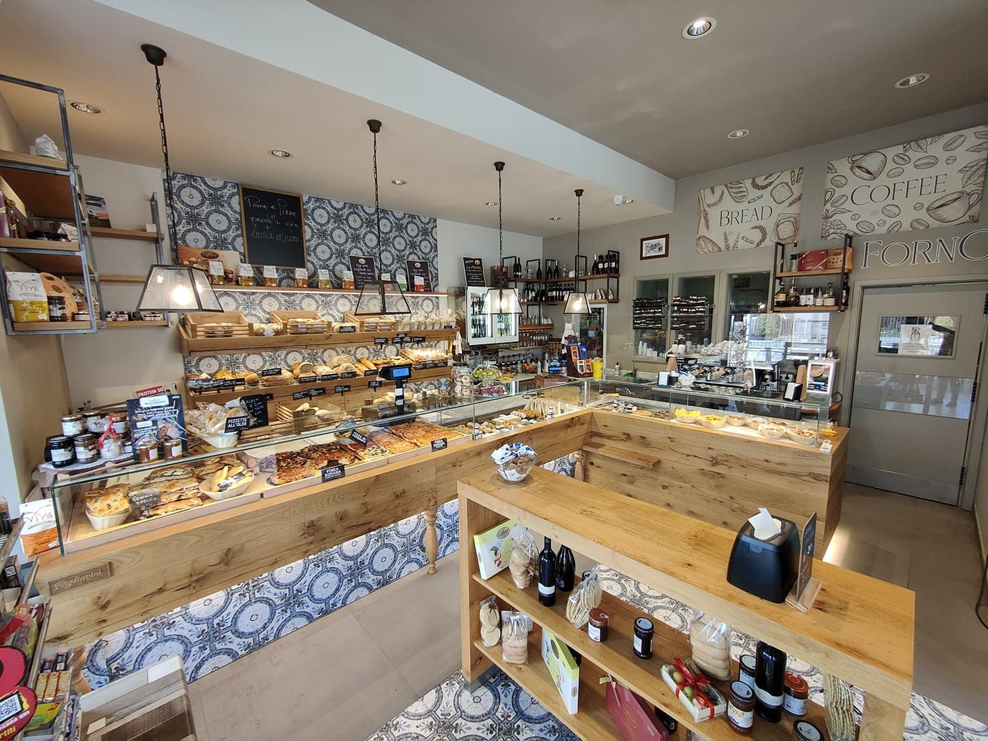 Interno di un panificio con banconi in legno pieni di pane e pasticcini, sullo sfondo di piastrelle decorative blu e bianche.