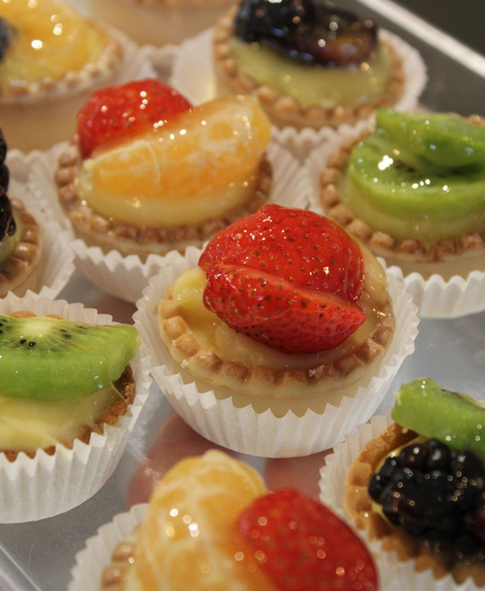Un assortimento di piccole crostatine di frutta con crema pasticcera, confezionate in pirottini di carta e guarnite