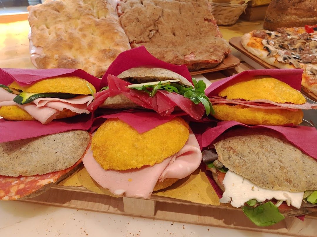 Su un bancone sono esposti diversi tipi di panini e focacce, con affettati, verdure e panini colorati.