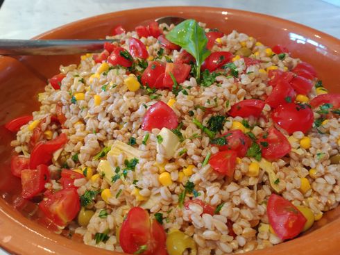 Una ciotola di terracotta riempita con un'insalata fresca di cereali contenente pomodorini, mais,