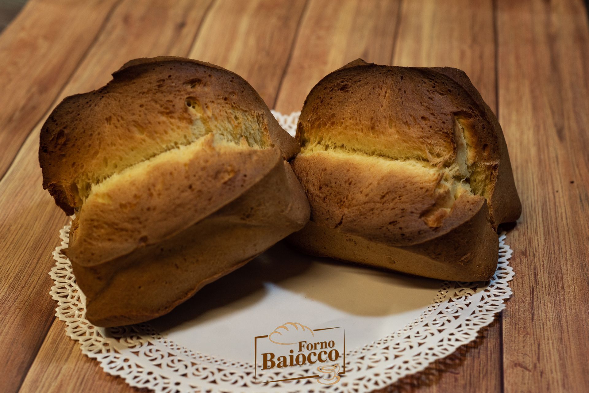 Due pagnotte di pane color marrone dorato poggiano su un centrino di pizzo bianco sopra una superficie di legno