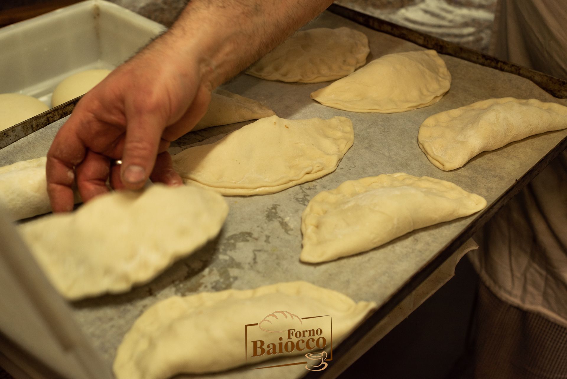 Una persona dispone delle sfoglie di pasta cruda a forma di mezzaluna su una teglia rivestita di carta da forno.