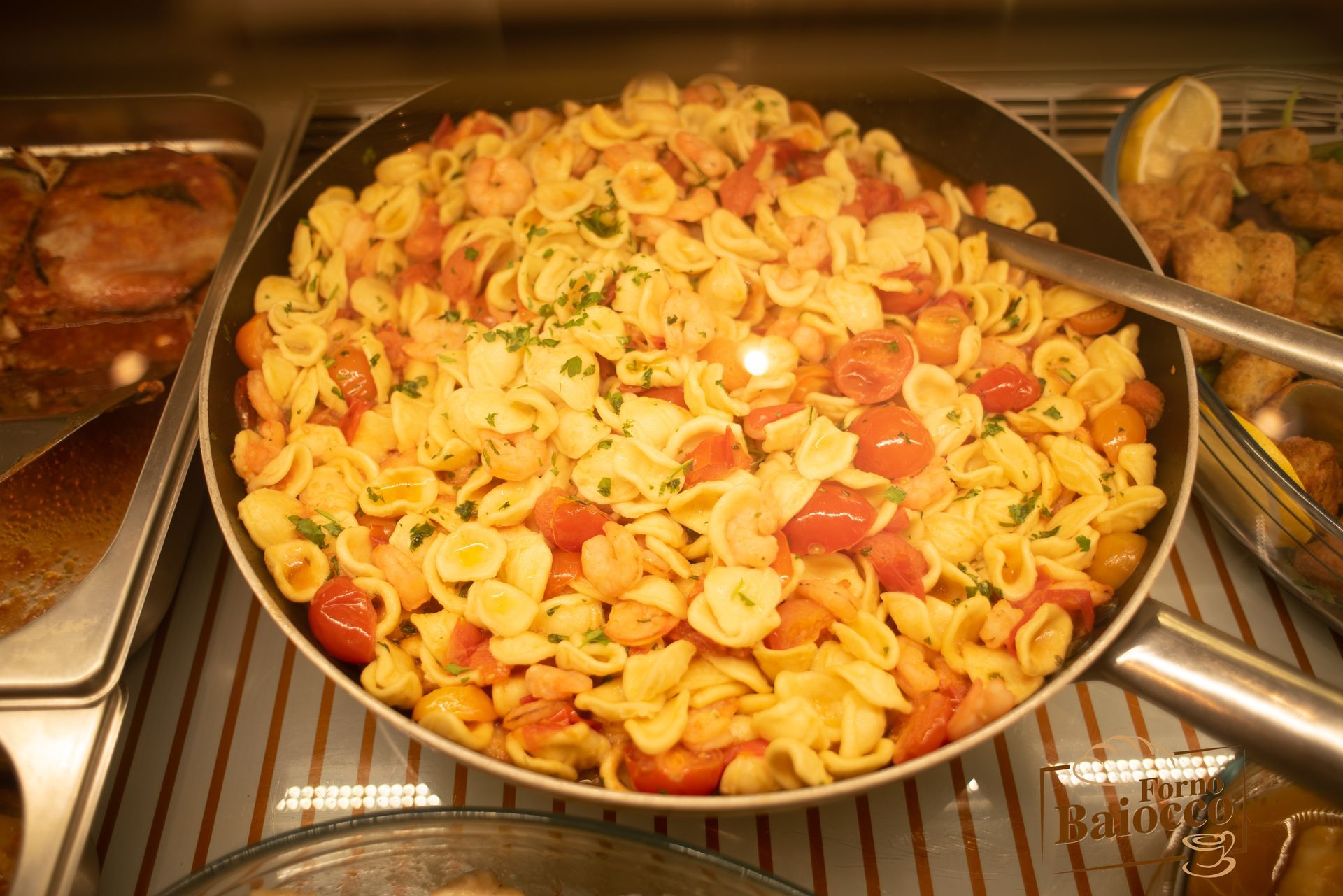 Una grande teglia di orecchiette condite con pomodorini e erbe aromatiche fresche