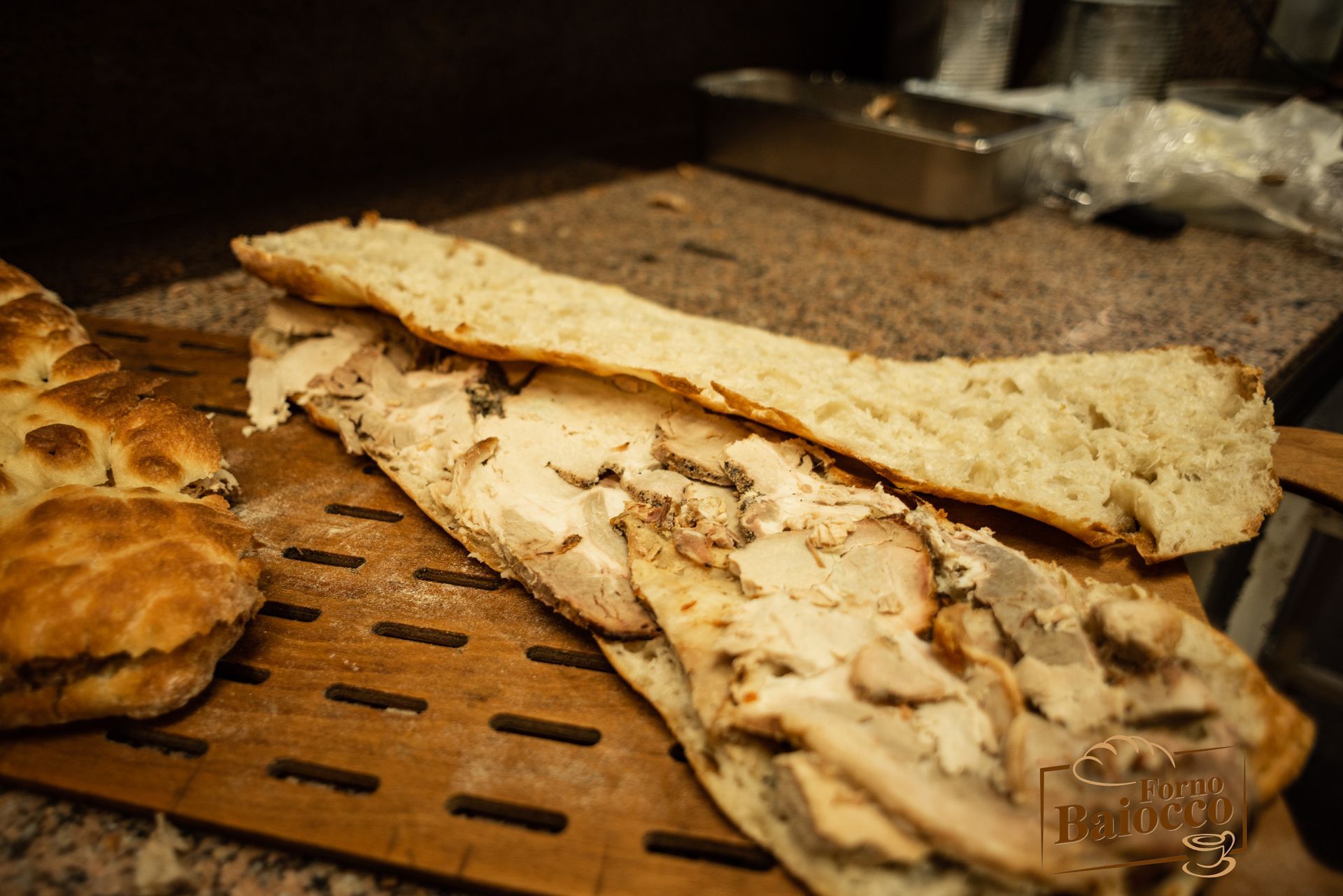 Un panino al pollo parzialmente assemblato su un tagliere di legno, con una fetta di pane appoggiata sopra.