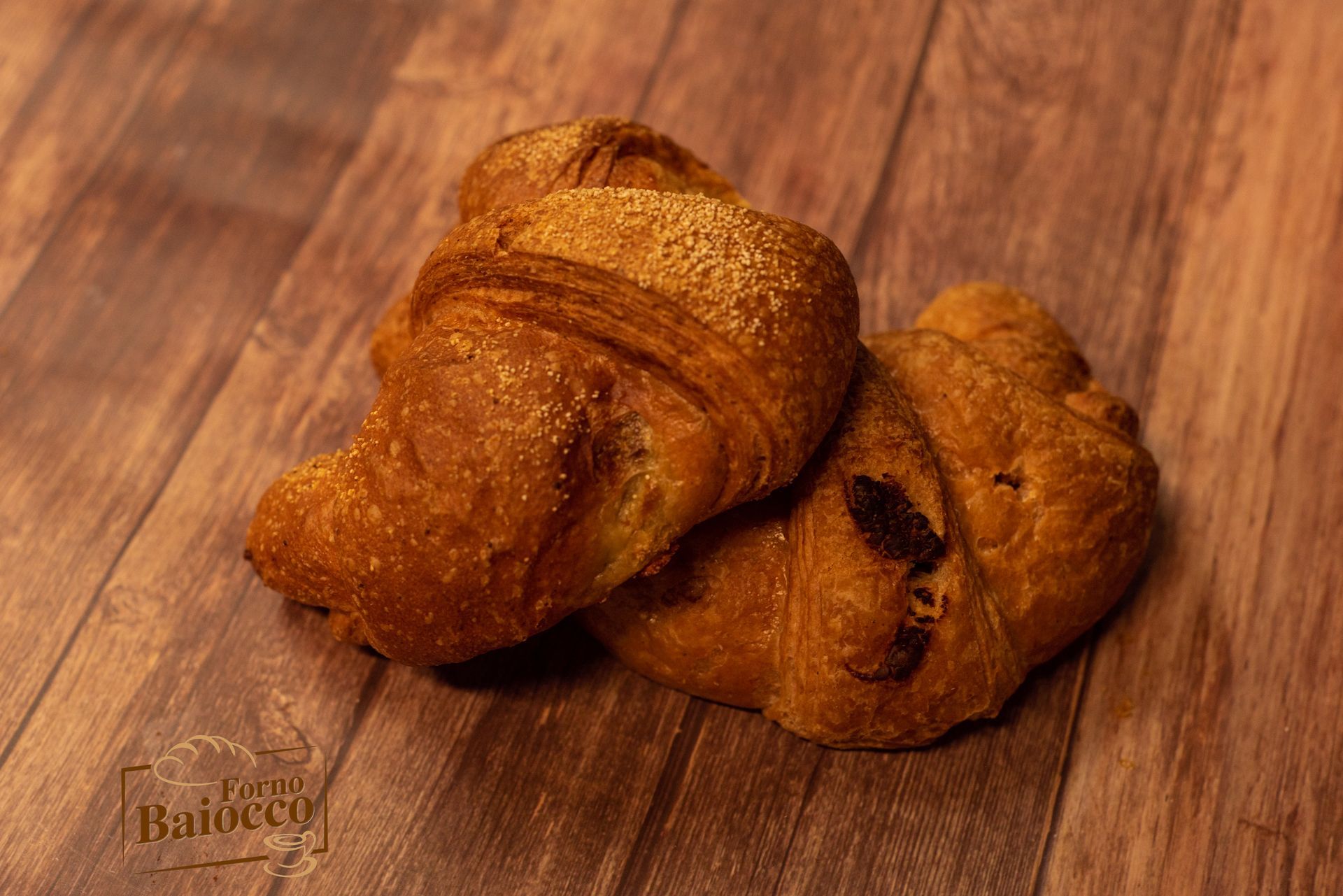 Due croissant dorati e friabili adagiati su una superficie con venature di legno scuro 
