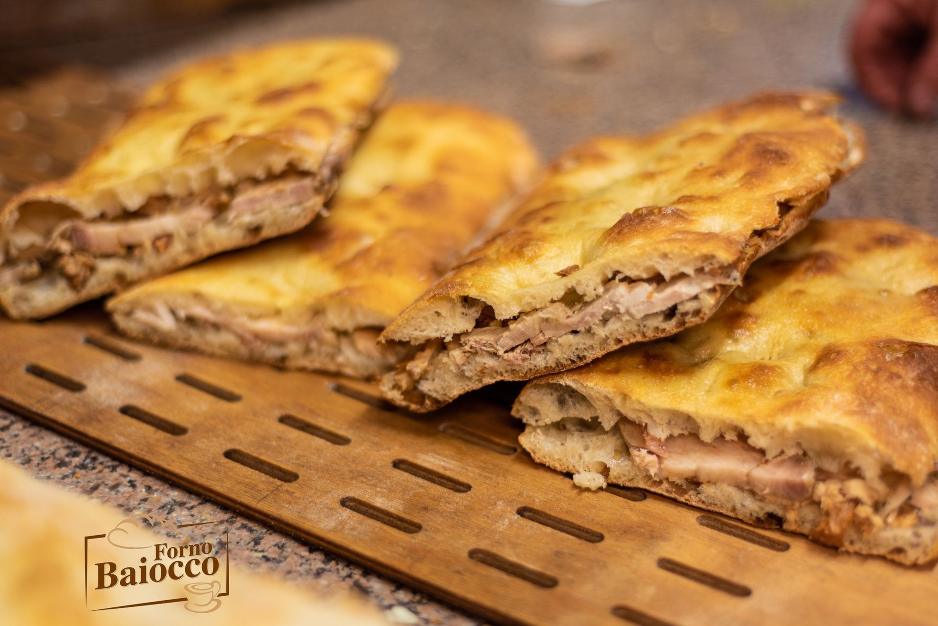 Diverse fette di focaccia dorata ripiene di carne, disposte su un tagliere di legno con un piccolo logo del ristorante.