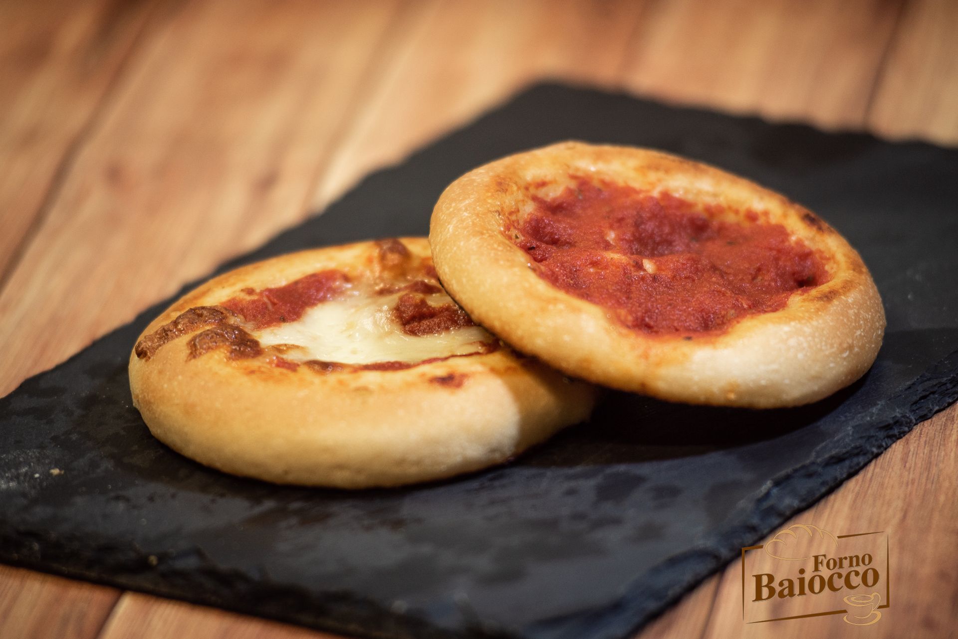 Due piccole pizze rotonde su un vassoio di ardesia nera, una con formaggio e salsa di pomodoro e l'altra solo con salsa.