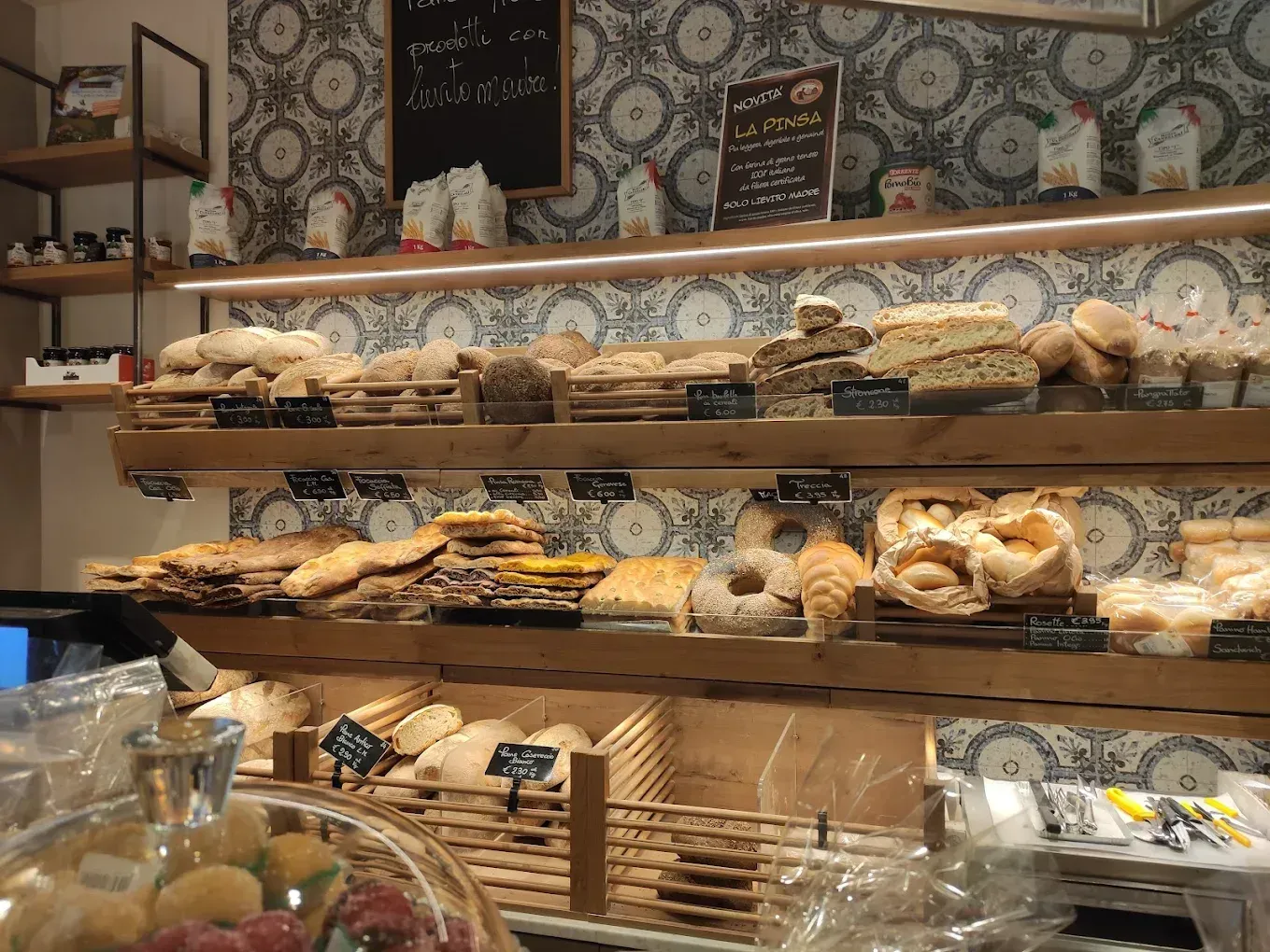Una vetrina da panetteria con ripiani in legno rifornita con vari tipi di pane, pasticcini e prodotti artigianali.