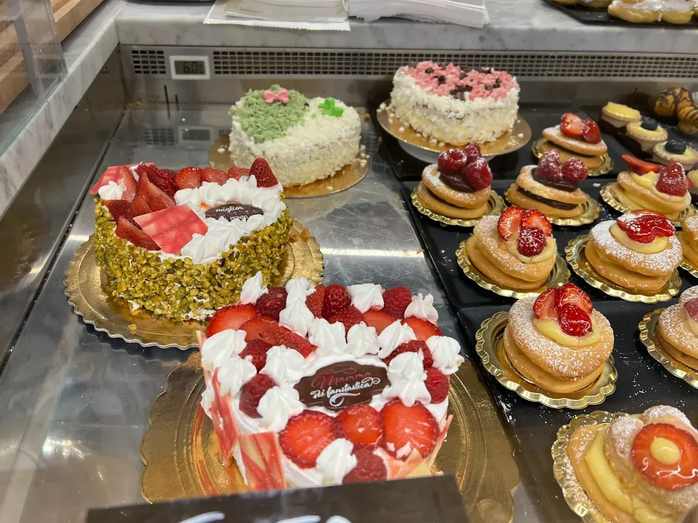 Una vetrina piena di torte e pasticcini di alta qualità, tra cui torte a forma di cuore e crostate di frutta.