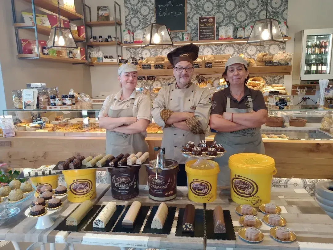 In una pasticceria, tre membri dello staff con il grembiule sono in piedi dietro un bancone pieno di cannoli