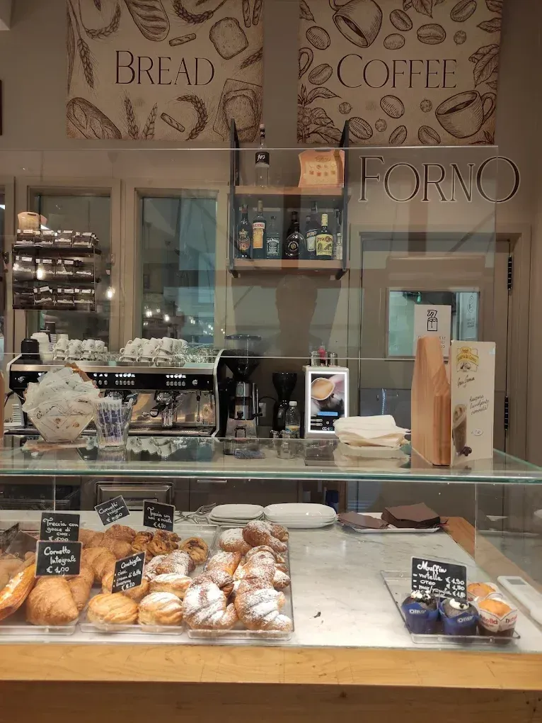 Il bancone di una panetteria espone i dolci sotto una parete di vetro, mentre sulla parete retrostante sono visibili 