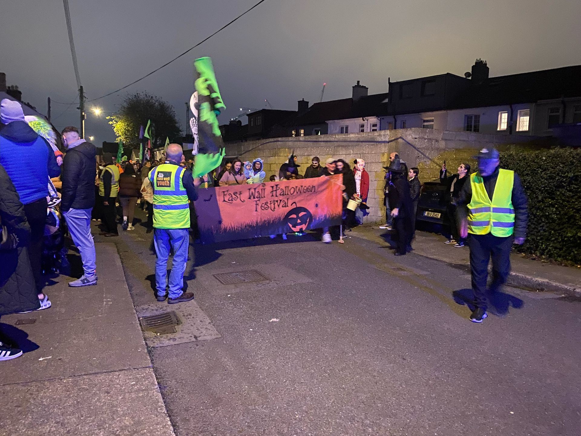 People marching down a street at dusk, carrying banners and flags. Some wear high-visibility vests.
