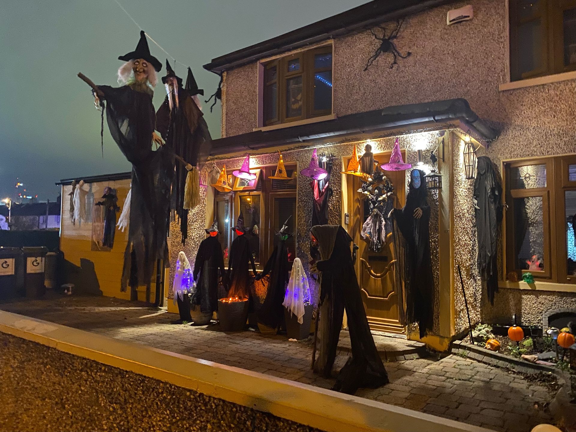 A house decorated for Halloween with witches, ghosts, and pumpkins, illuminated at night.