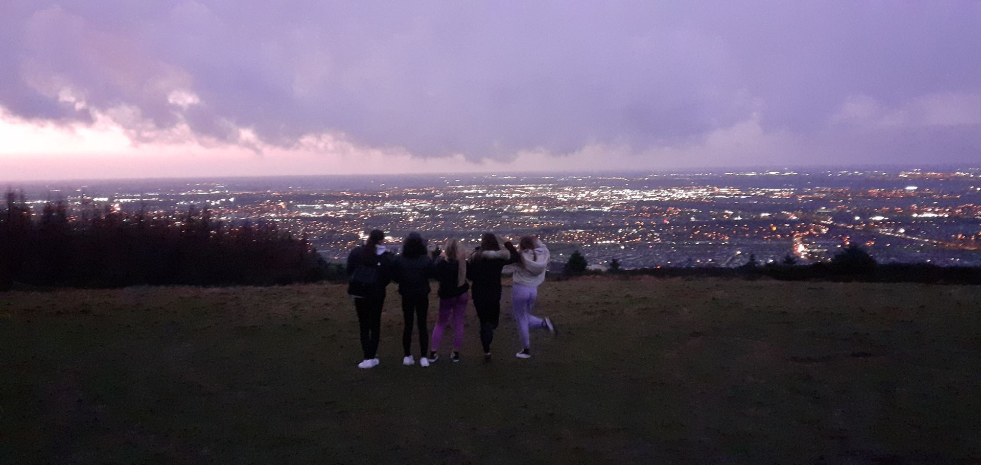 Five YP stand on a hill overlooking a city at dusk. They are silhouetted against the night sky, illuminated by city lights.