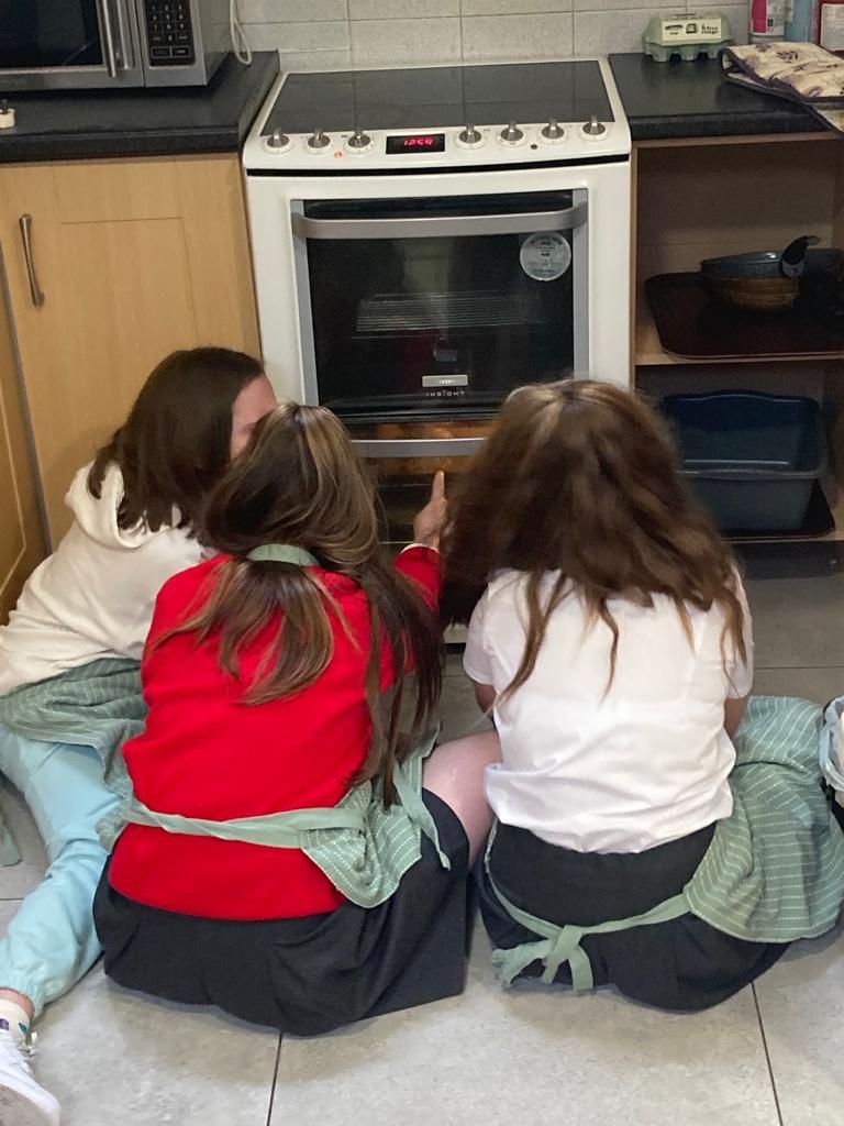 Three people looking at the inside of an oven. They're wearing aprons and are seated on the floor.