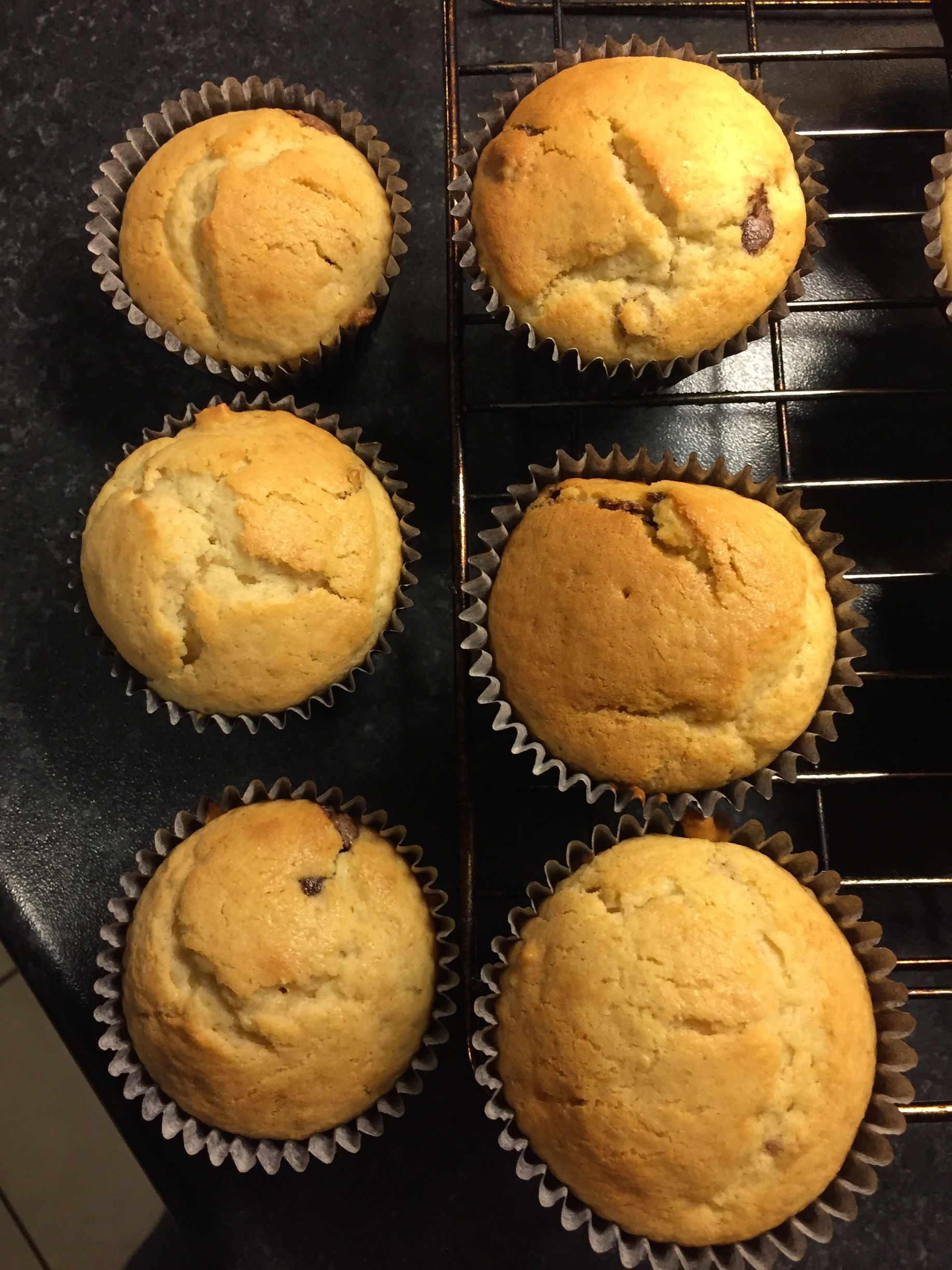 Six freshly baked muffins in paper liners on a cooling rack.