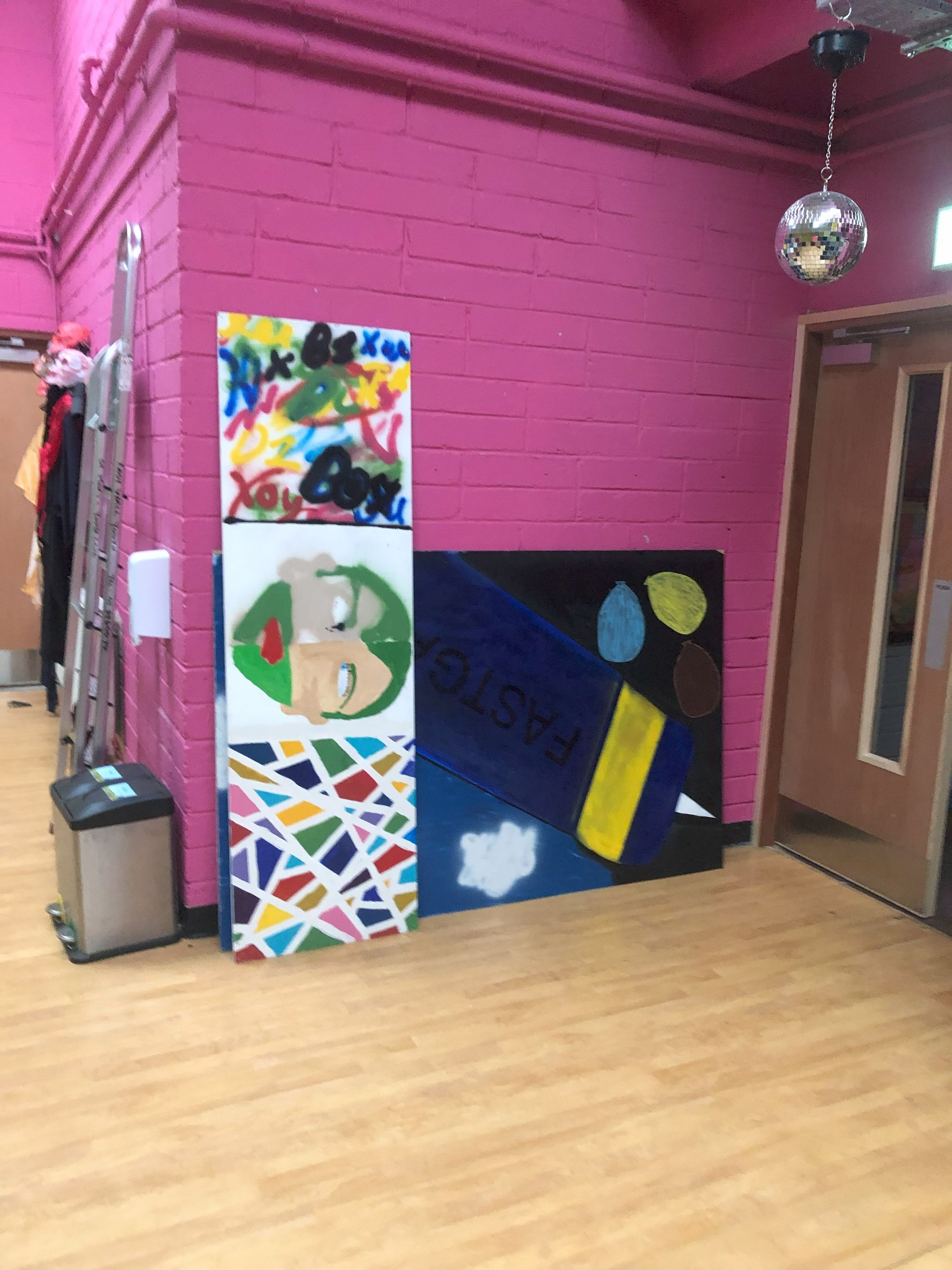 Artwork on pink wall, wooden floor; includes abstract paintings. A disco ball hangs from the ceiling.