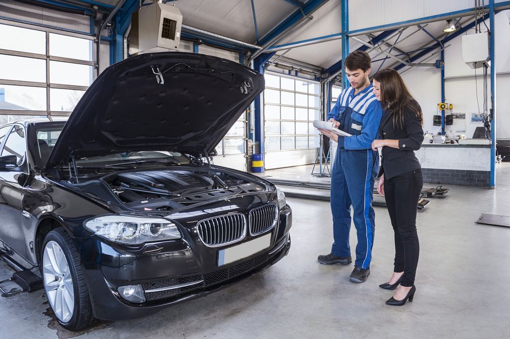 A man and a woman are looking at a car in a garage.