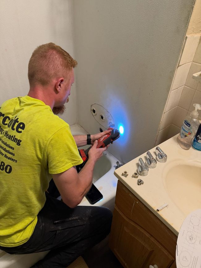 Technician inspecting a bathroom wall with a handheld device, blue light shining near a sink and cabinet