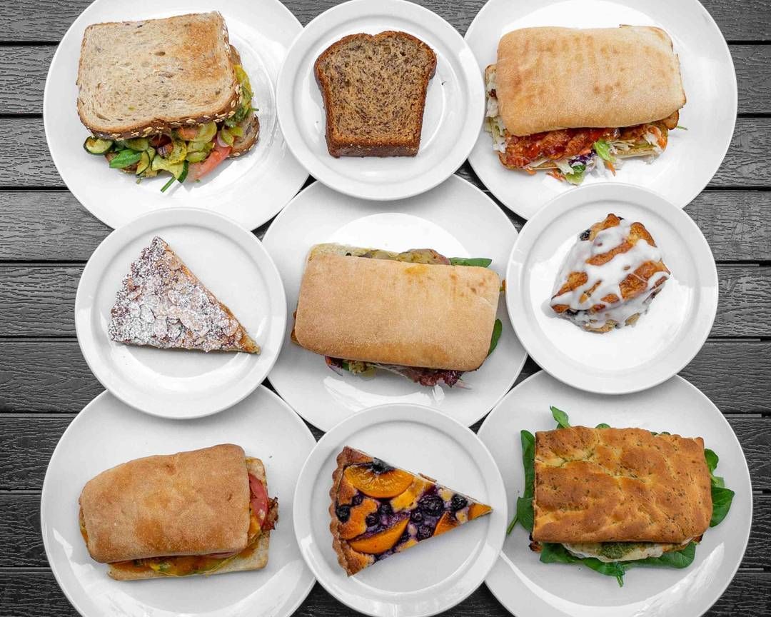 Plates of food: sandwiches, bread slice, pie, and pastry on a gray wooden table.