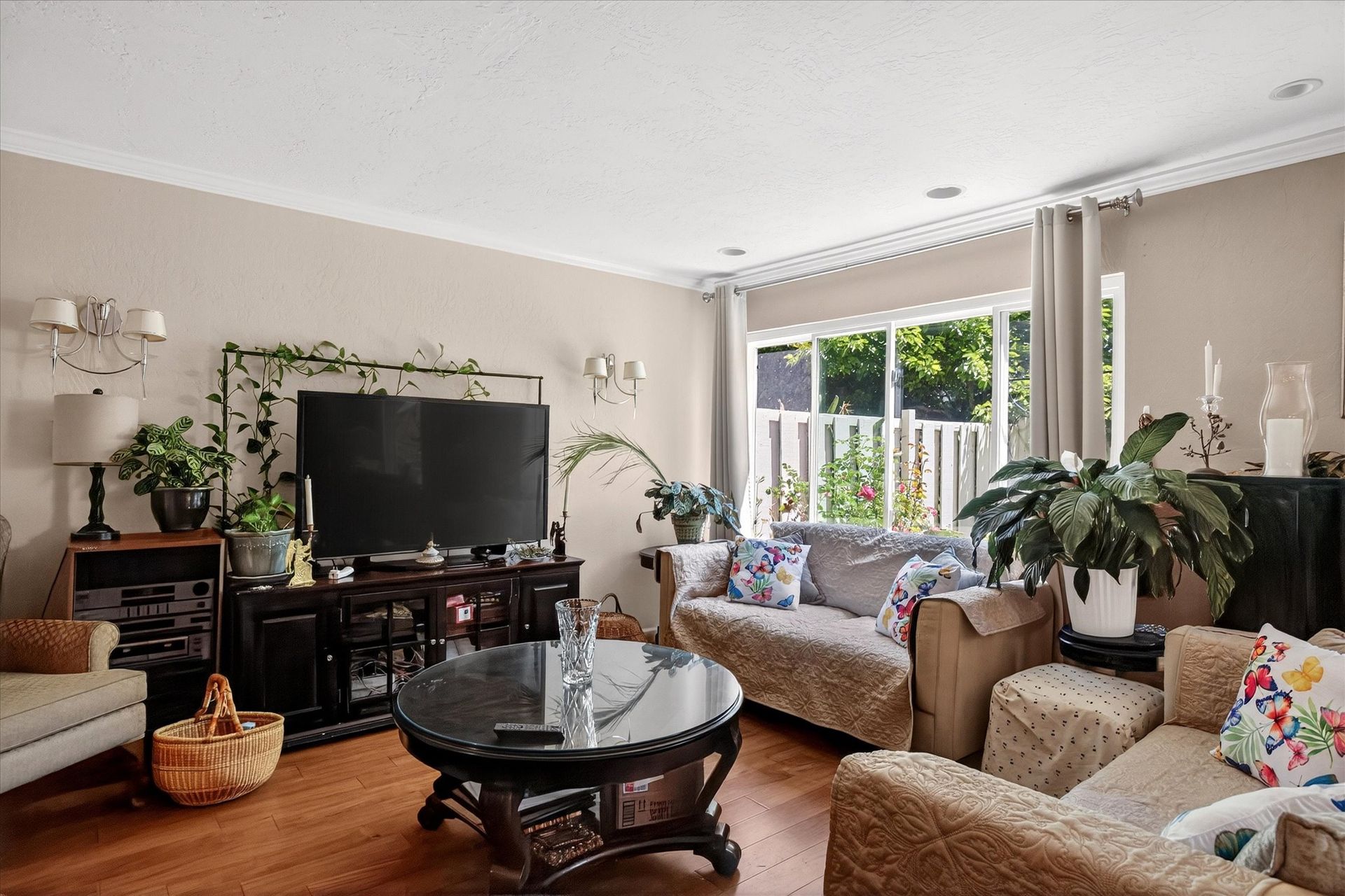 Bright living room with beige sofas, a large TV, coffee table, houseplants, and sunlight by the window