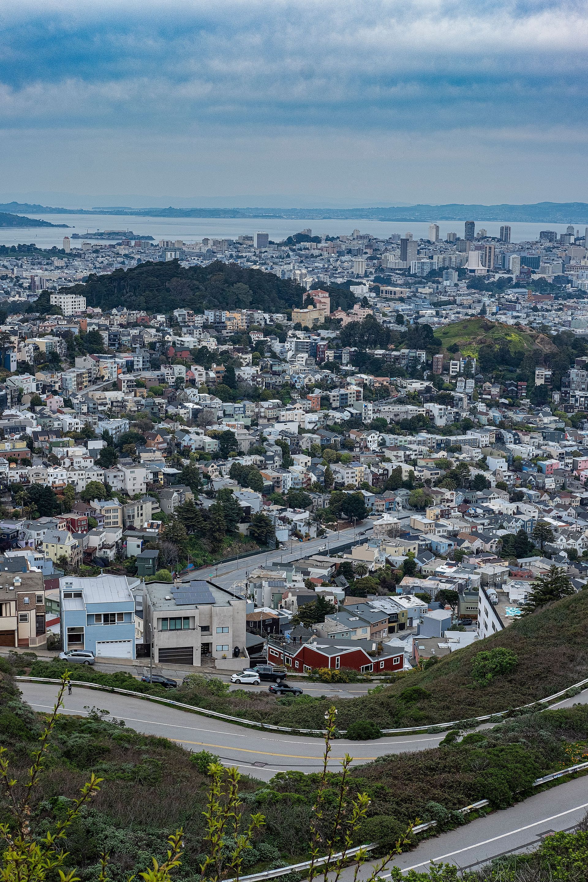 Hillside view of a dense coastal city under a cloudy sky, with winding roads in the foreground