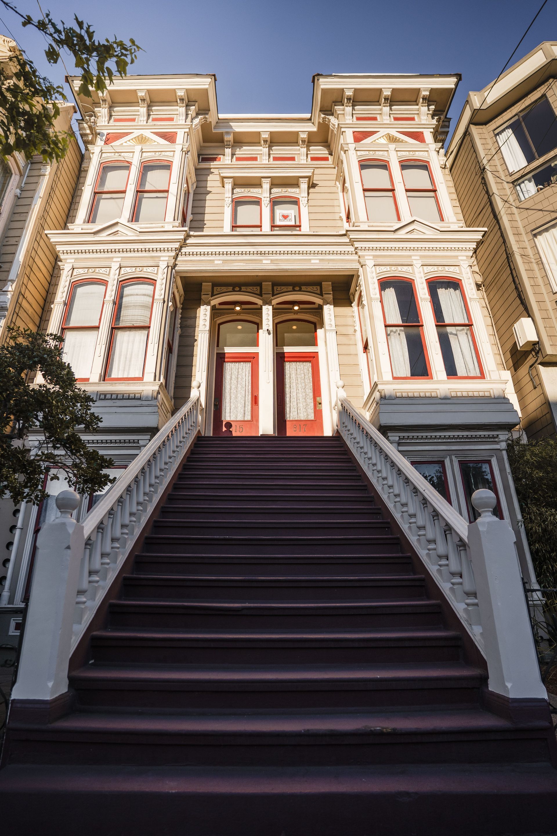 Victorian house with ornate white trim and red doors, viewed from the bottom of a steep staircase