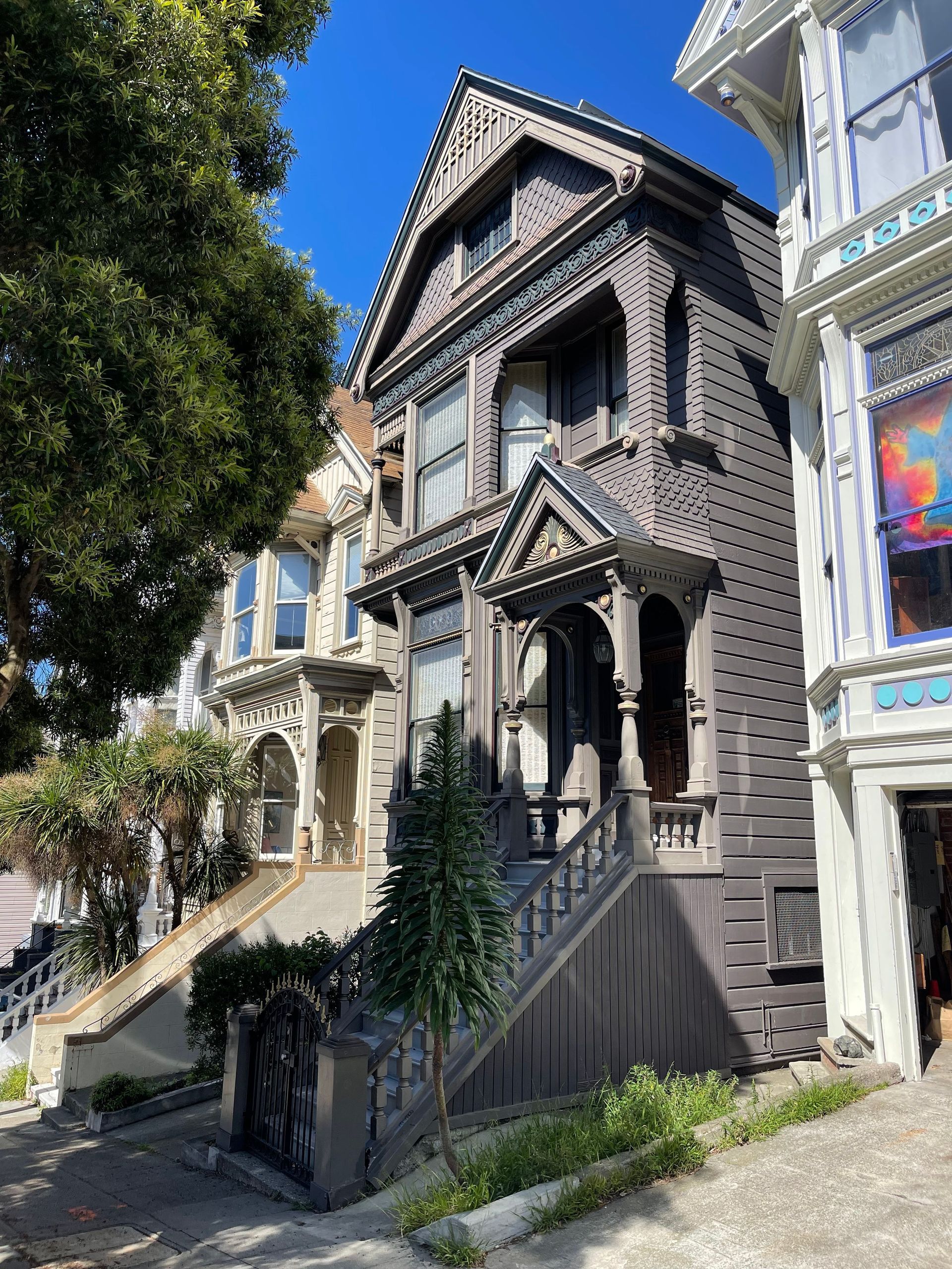 Victorian-style dark gray house with ornate wood trim and steep gabled roof on a sunny city street