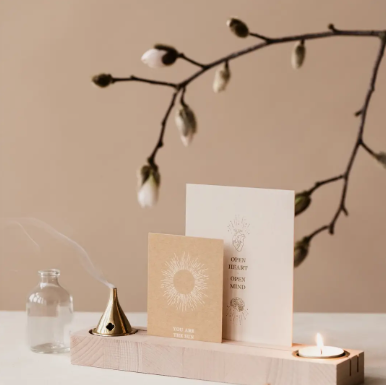 Minimalistisch beige altaar met kaarten, kaars, wierook en een gedroogde tak op een houten dienblad.