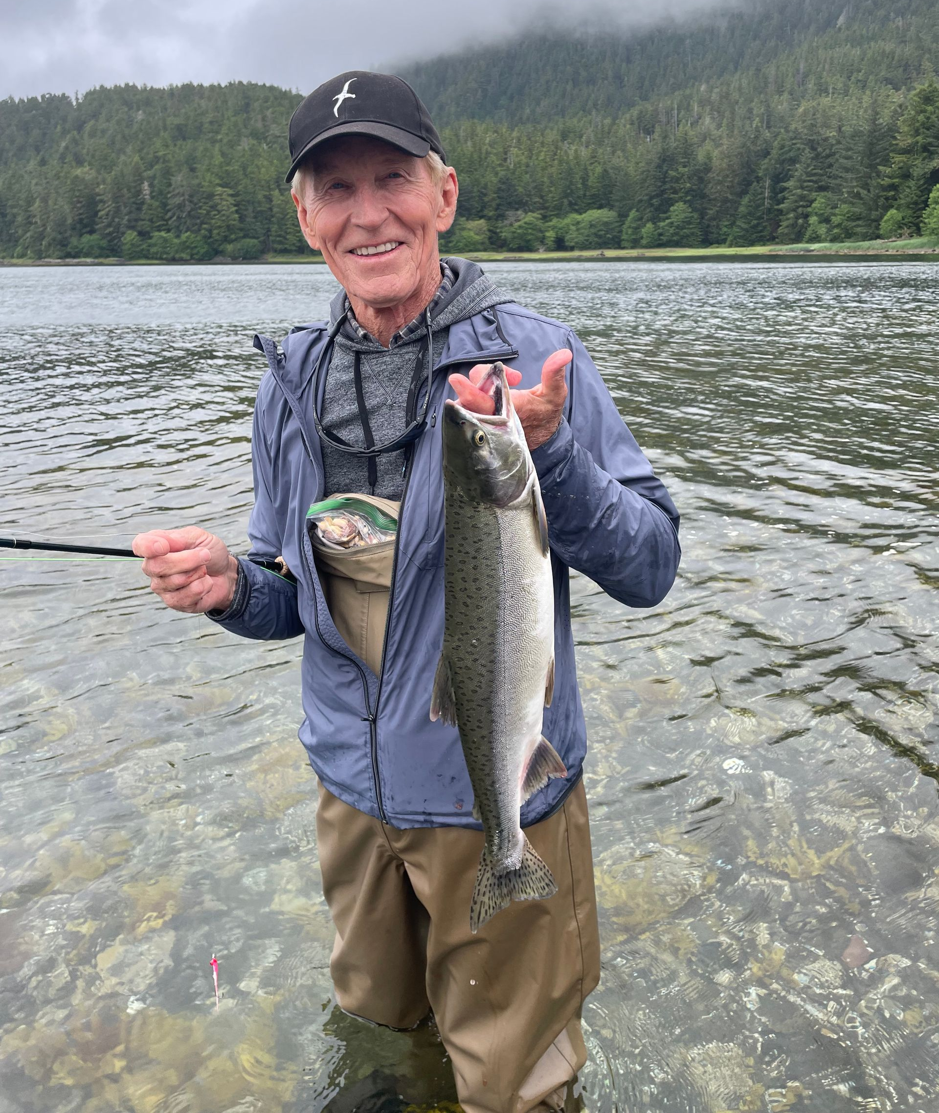 Smiling angler in a blue jacket holds a large fish in a shallow mountain lake
