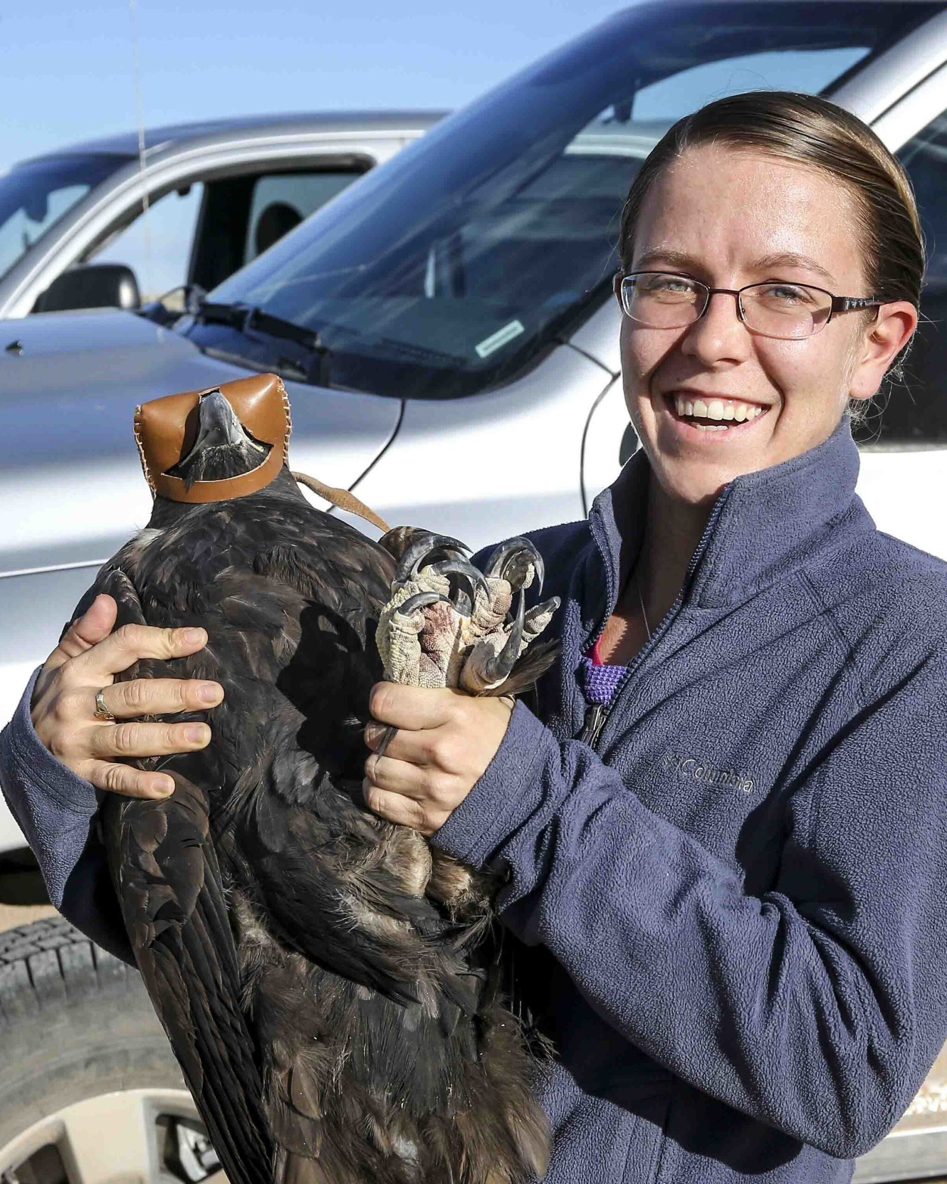 Woman holding a black-and-brown cat in front of parked cars, smiling outdoors