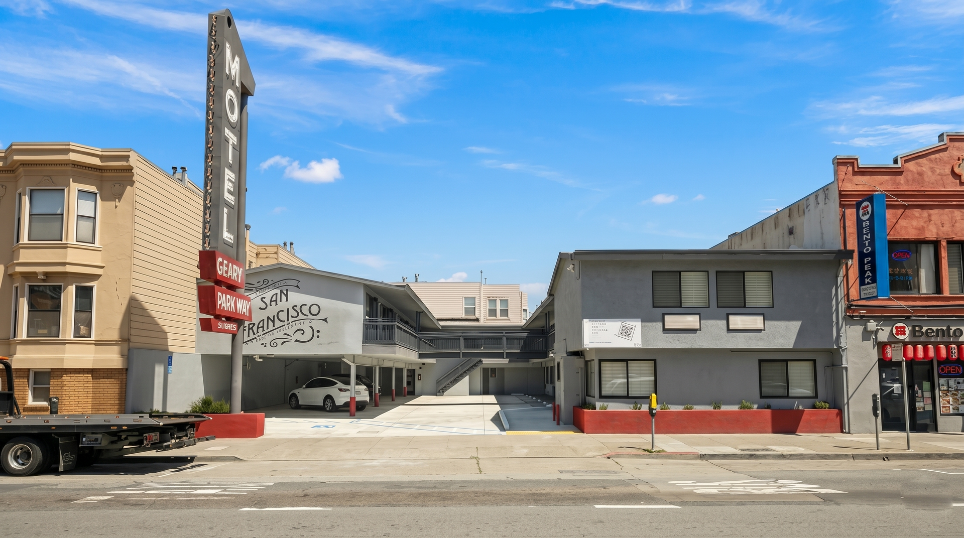 City street with parked truck, red-brick and gray storefronts, and a tall vertical sign under a blue sky
