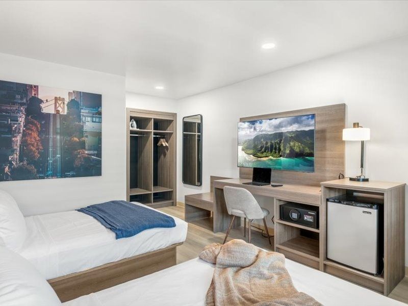 Modern hotel room with bed, desk, TV, open closet, and city wall art