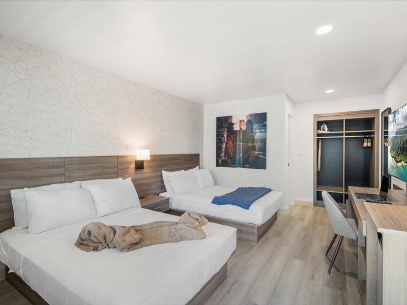 Modern hotel room with two beds, desk, wardrobe, and soft neutral decor