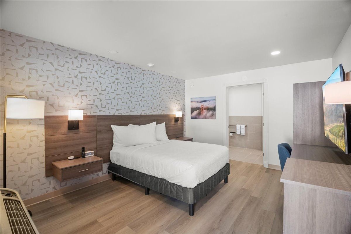 Modern bedroom with a bed, nightstands, wall lights, TV, and a bathroom doorway