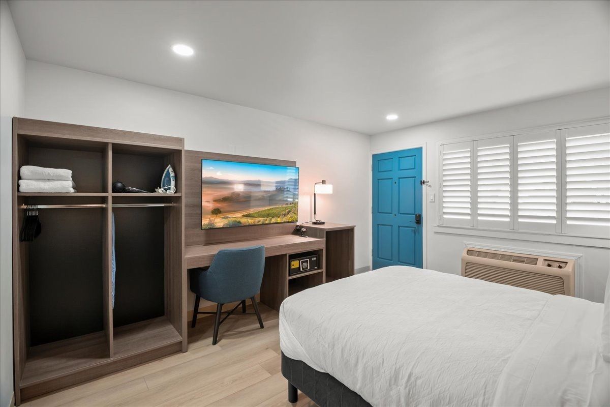 Bright bedroom with desk, blue door, white shutters, and neatly made bed