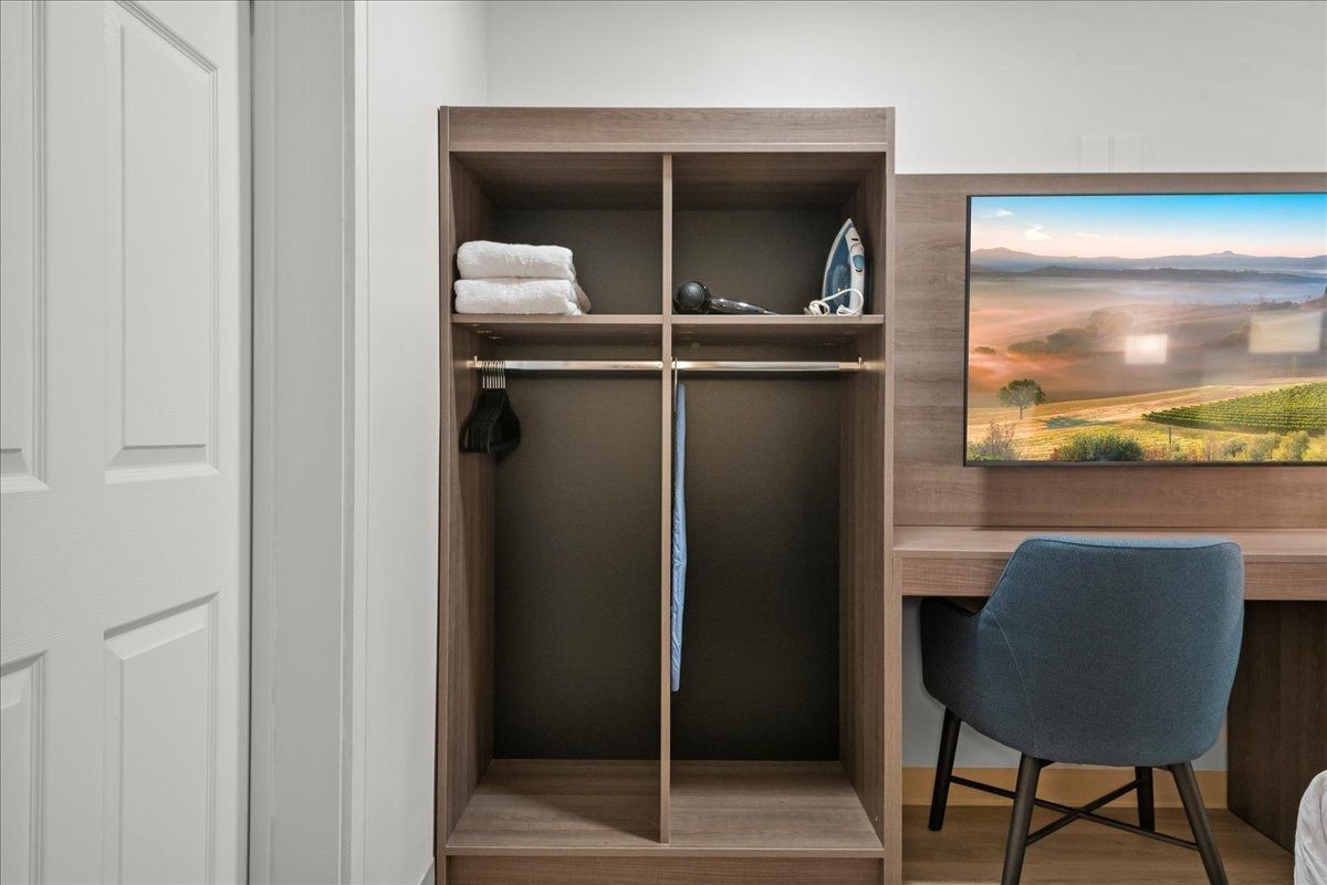 Open closet with shelves and hanging space beside a desk, chair, and wall-mounted landscape screen.