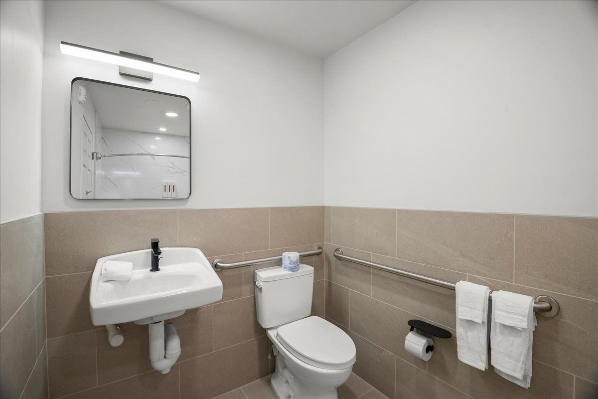 Accessible restroom with wall-mounted sink, toilet, grab bar, and beige tile walls