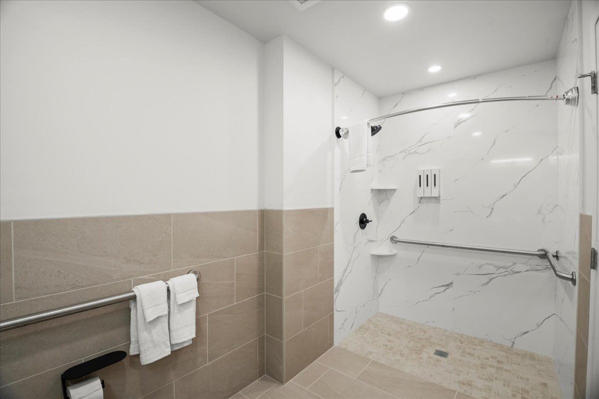 Accessible bathroom with beige tile, towel bar, and a walk-in shower with marble-pattern walls