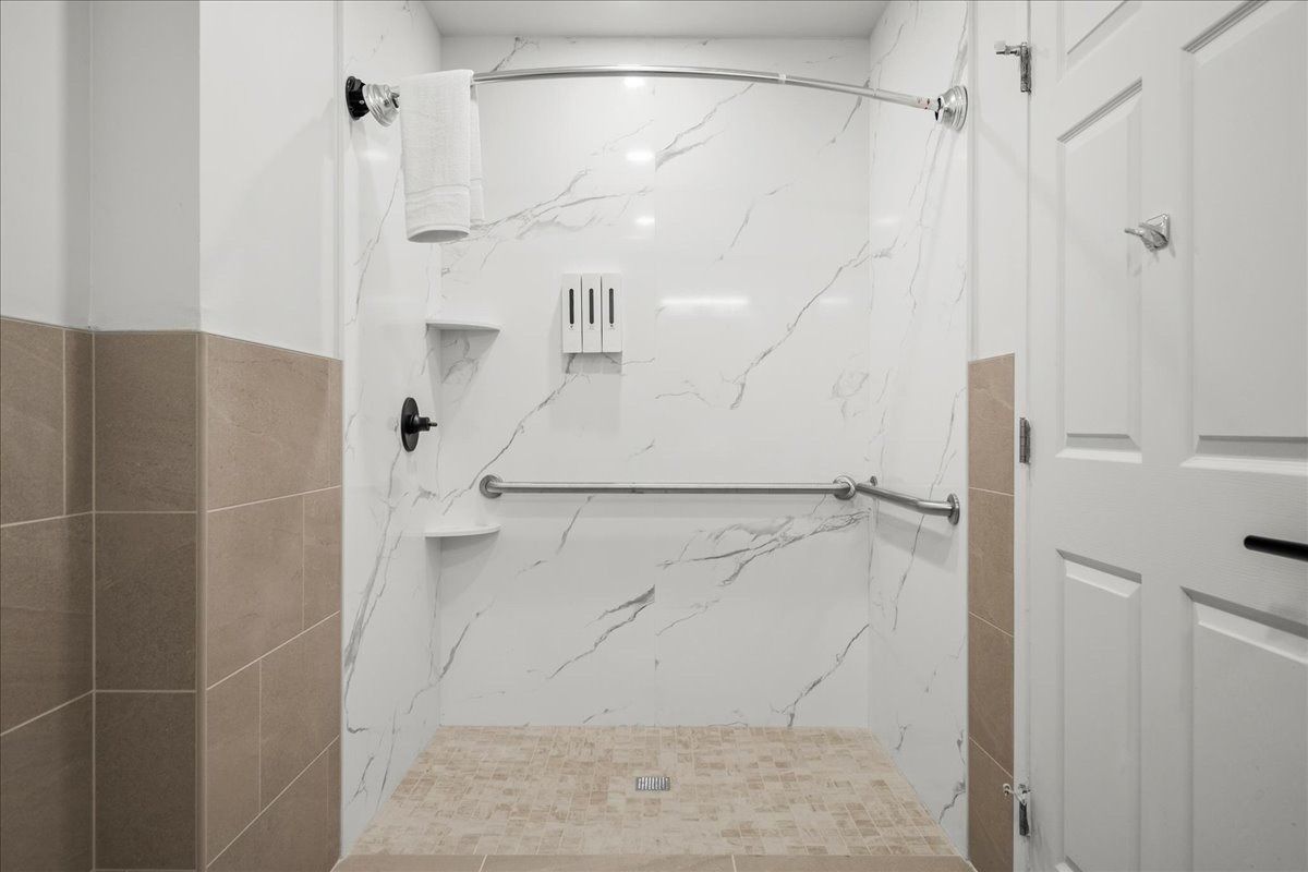 Empty tiled bathroom shower with white marble-look walls, built-in shelf, and beige floor tiles